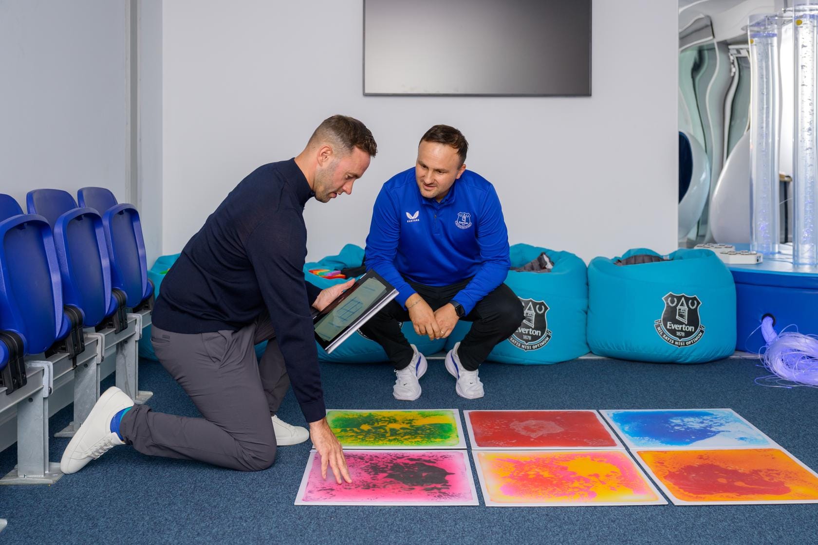 Two people review colourful tactile floor panels in Everton's sensory room